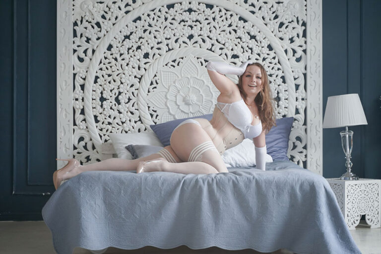 Plus Size Model in weißen Dessous liegt im Bett